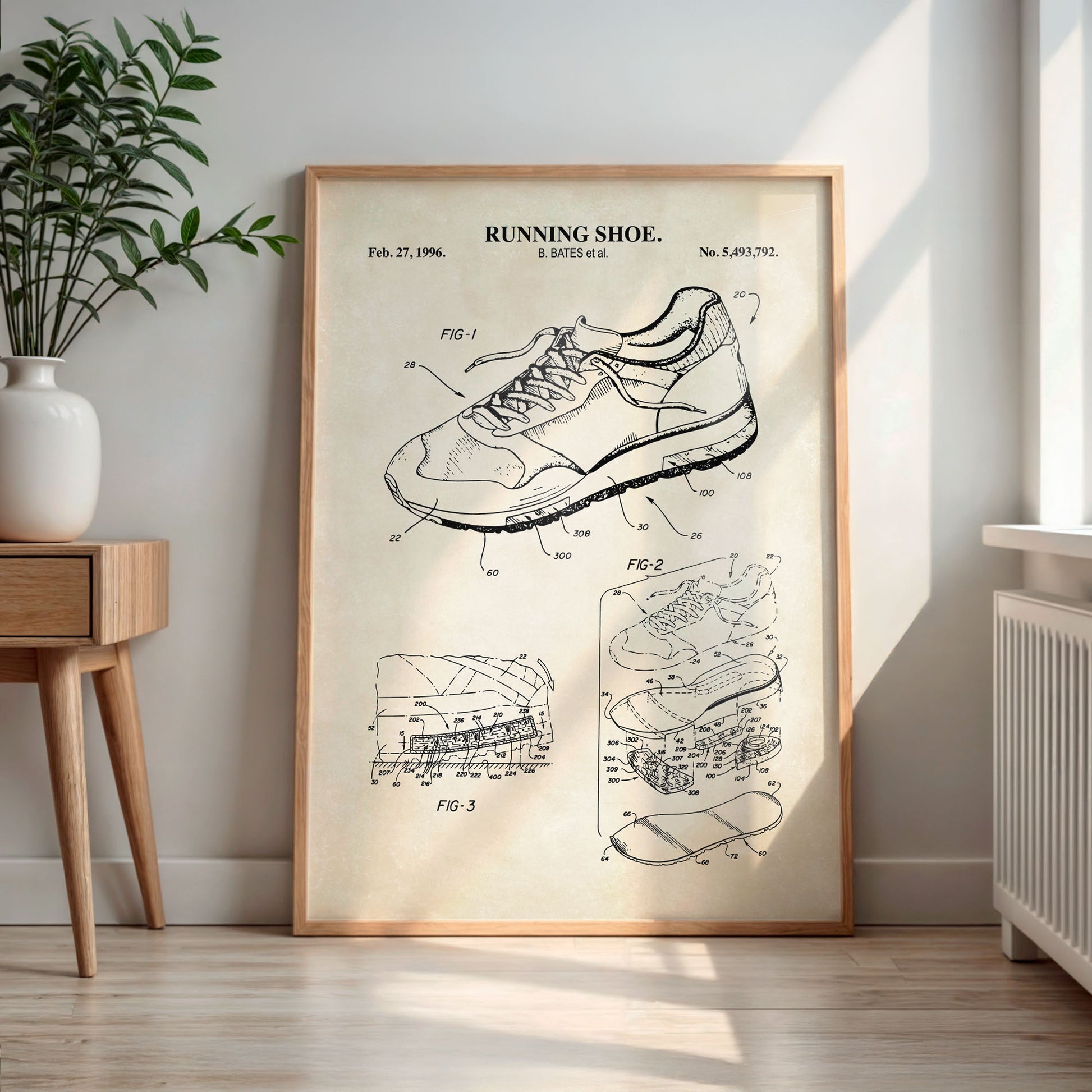 Framed poster of a running shoe patent in a room with a plant and wooden side table.