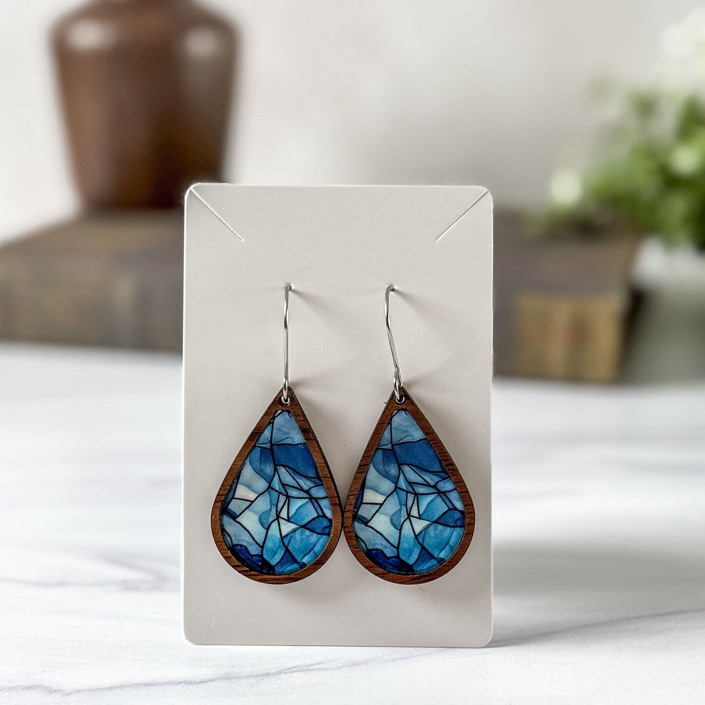 Teardrop-shaped blue and brown earrings on a white card with a blurred background