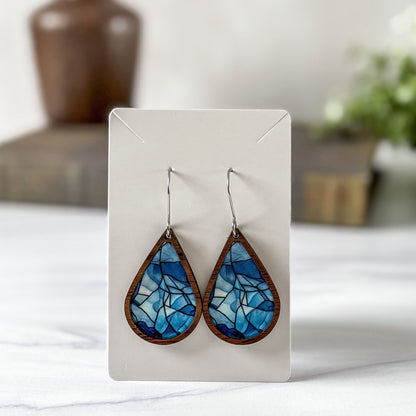 Teardrop-shaped blue and brown earrings on a white card with a blurred background