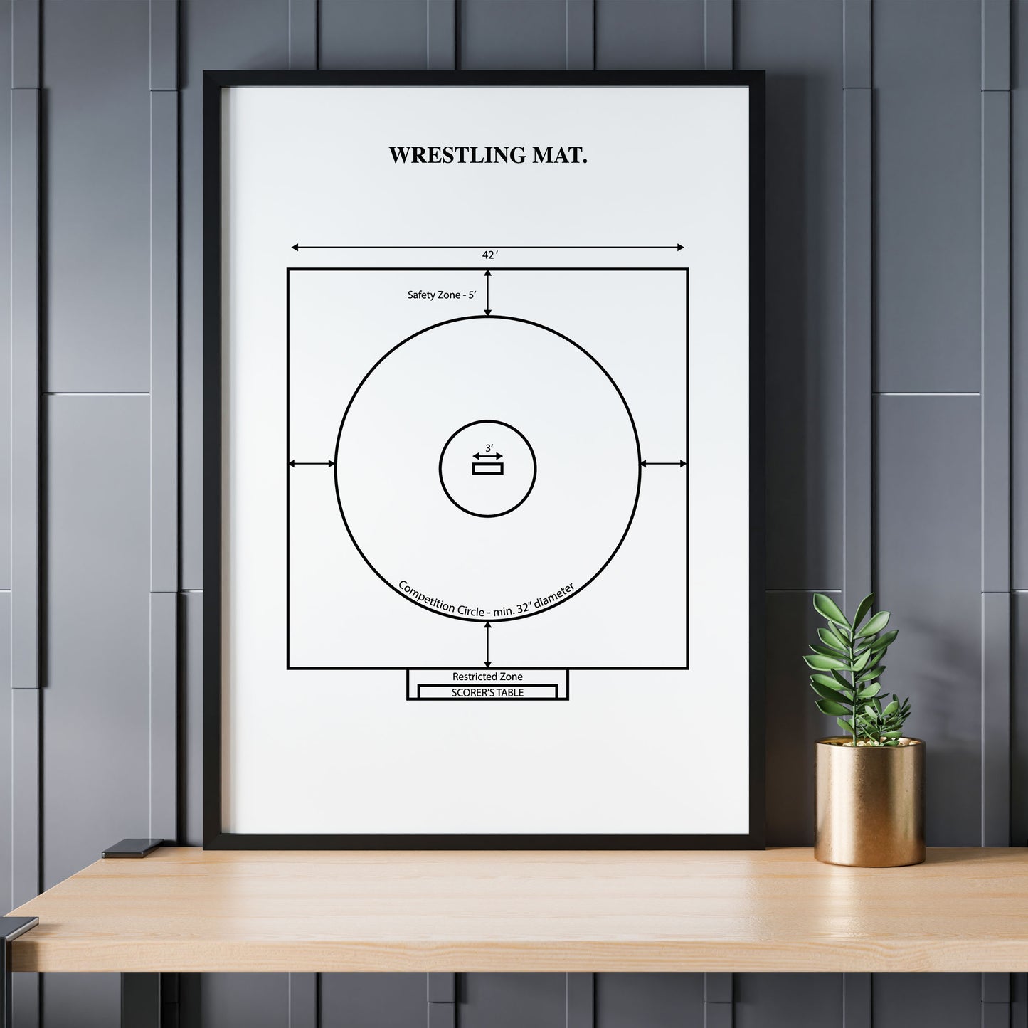 Framed poster of a wrestling mat diagram on a wall above a wooden table with a plant.