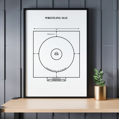 Framed poster of a wrestling mat diagram on a wall above a wooden table with a plant.