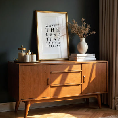 Wooden sideboard with framed quote - what's the best that could happen - and decorative items against a dark wall