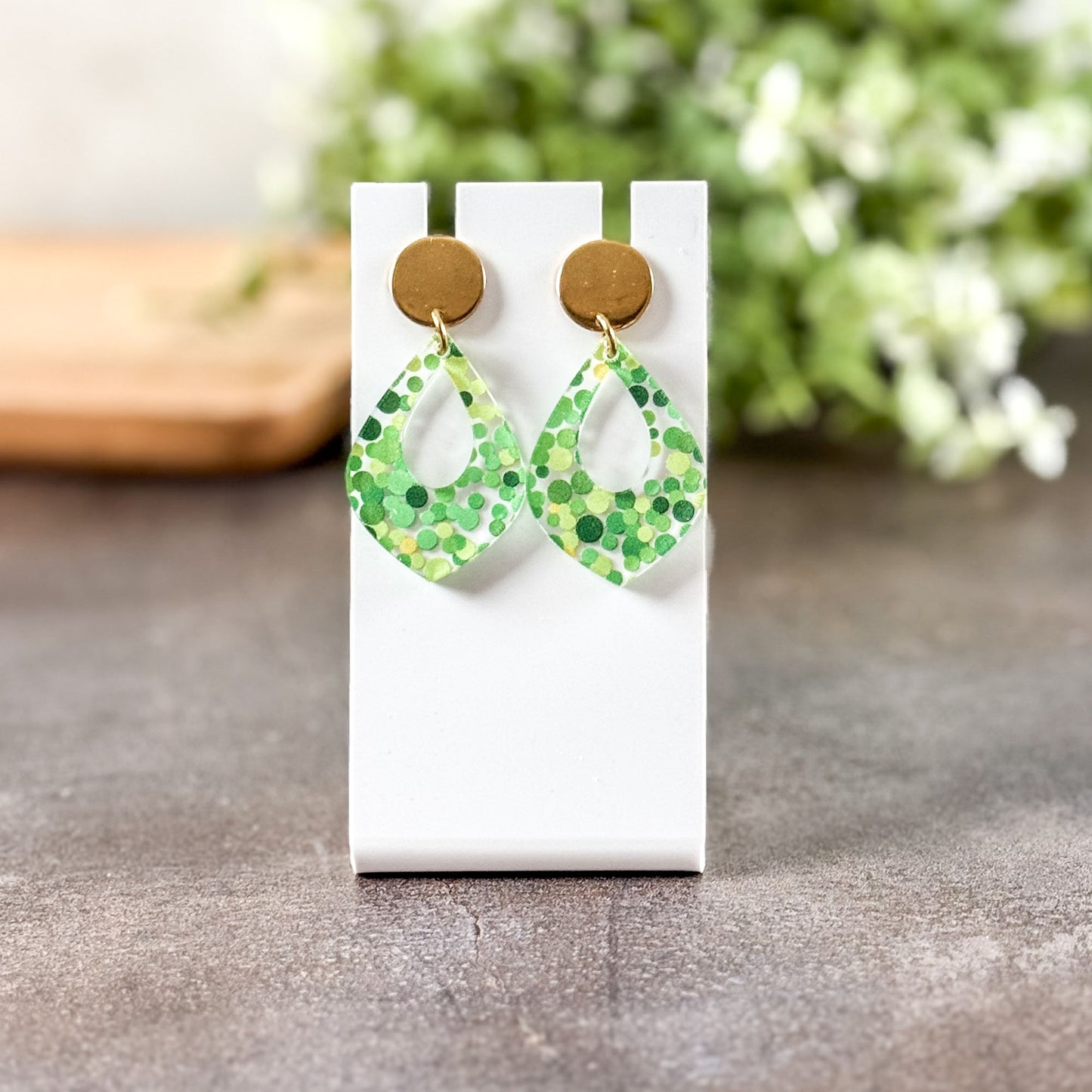 Green patterned earrings on a white card with a blurred natural background
