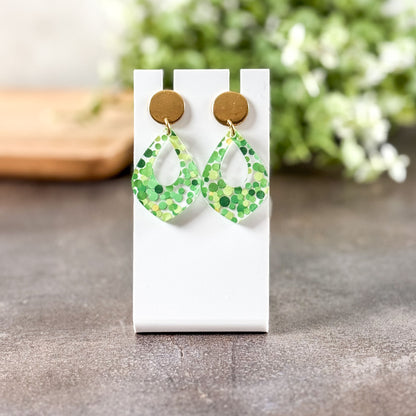 Green patterned earrings on a white card with a blurred natural background