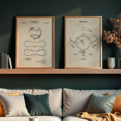 Two framed vintage baseball field patent prints hang on a dark green wall above a sofa with neutral-toned pillows and a throw blanket. A wooden shelf with books and dried flowers is visible below.