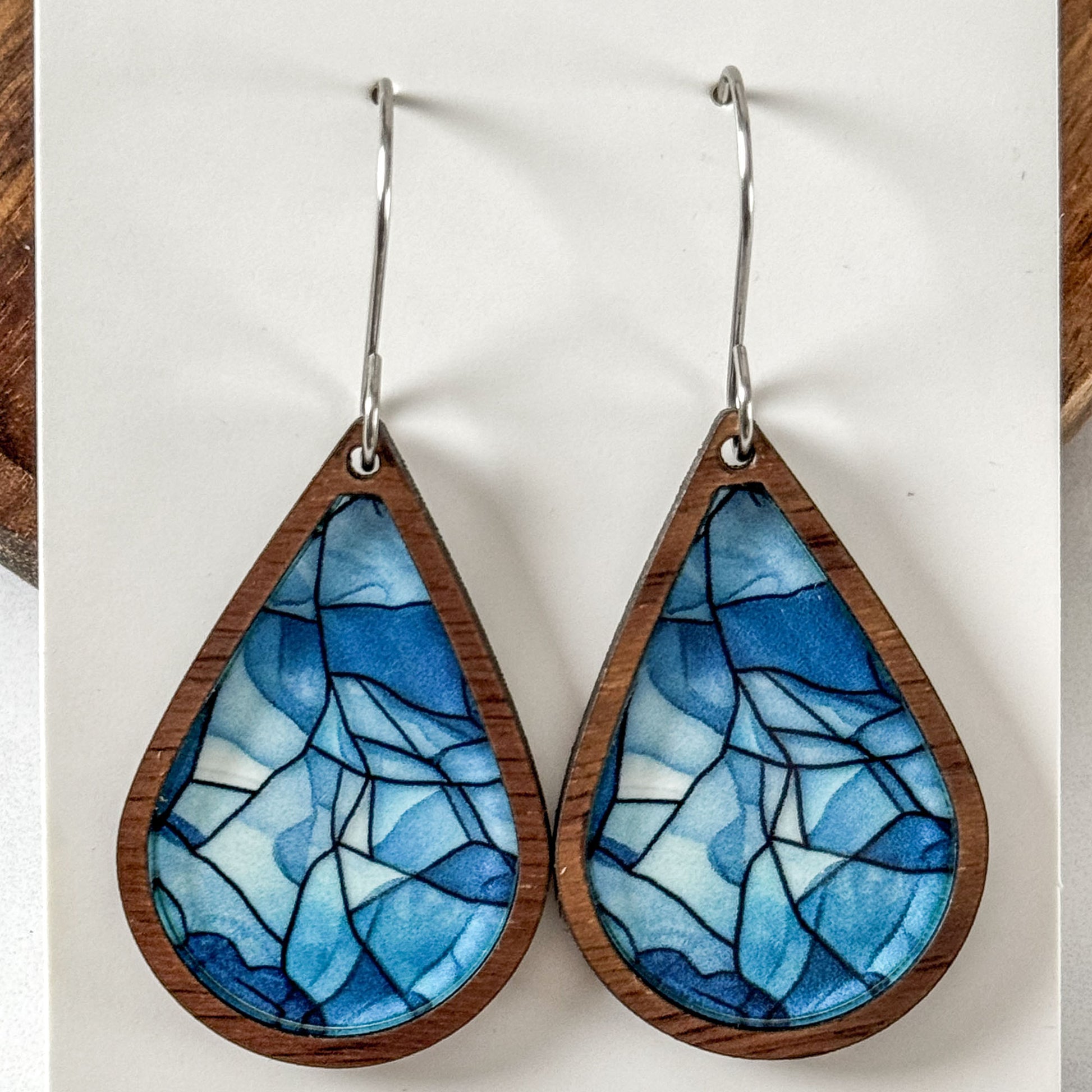 Teardrop-shaped earrings with blue stained glass design on a wooden background
